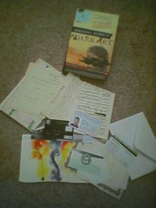 The new book by JC Hutchins and Jordan Weisman, shown with the pile of extras that come with the text to begin the immersion experience in the novel's story.